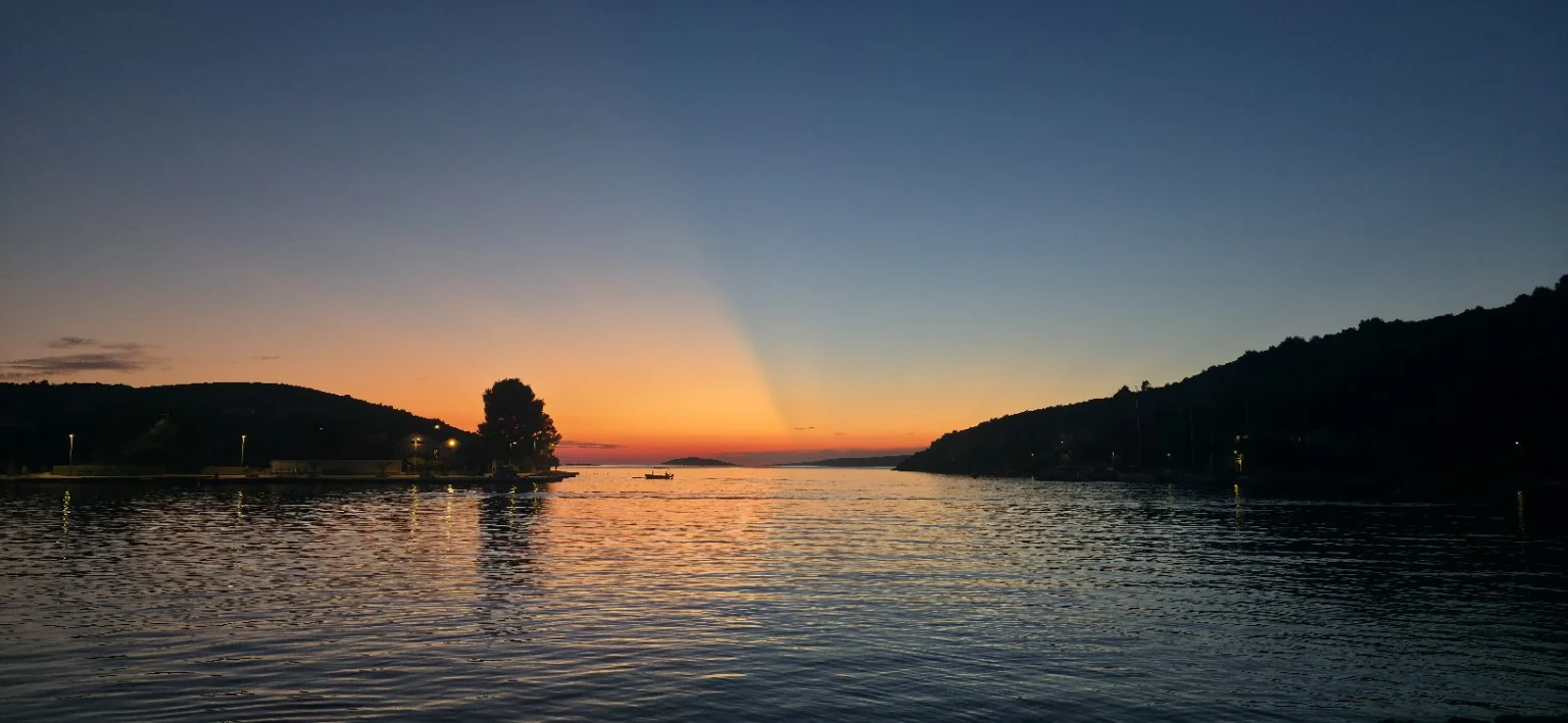 Orange sunset across calm water between dark coastal hills