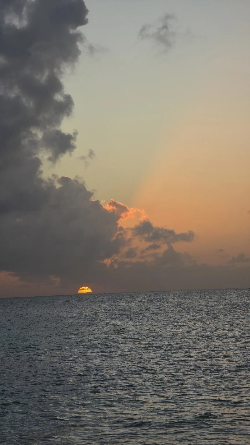 Sun setting on the horizon over open sea beneath dramatic clouds